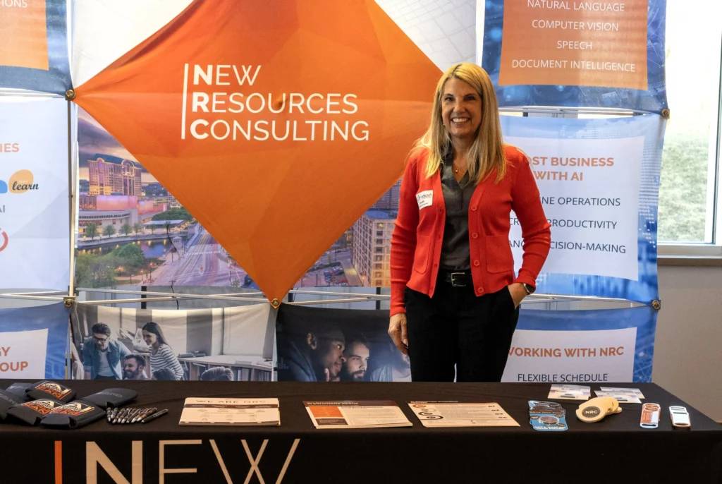 Professional woman standing at New Resources Consulting booth with informational materials and branded items.