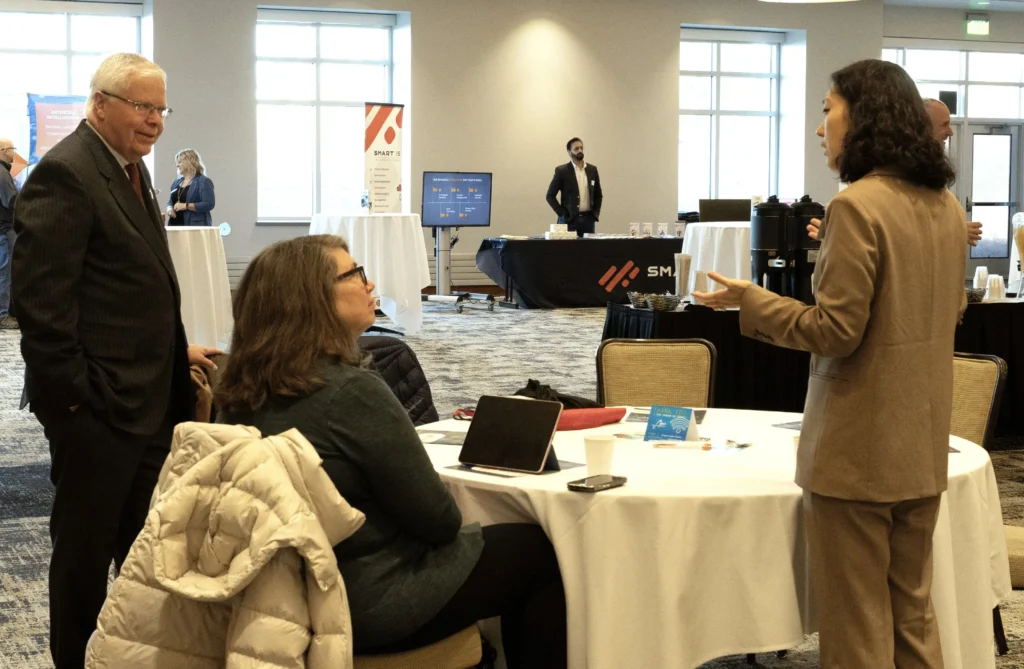 Professionally dressed individuals engaged in conversation around a round table in a conference room.