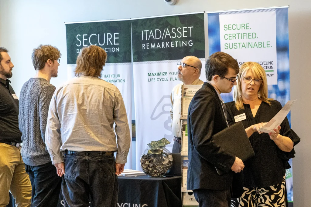 Professionally dressed individuals conversing at a secure data destruction and IT asset remarketing booth.