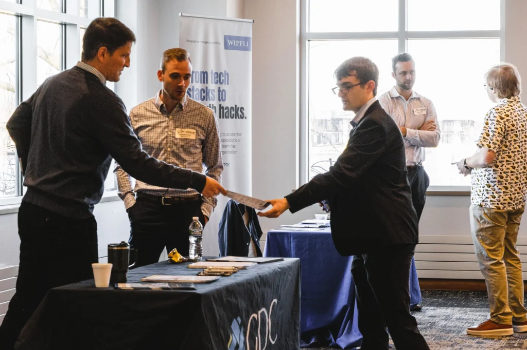 Professionally dressed men exchanging documents at a business networking event.