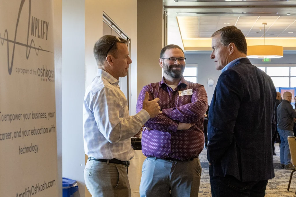 Three men in business casual attire engaged in conversation at an indoor networking event.
