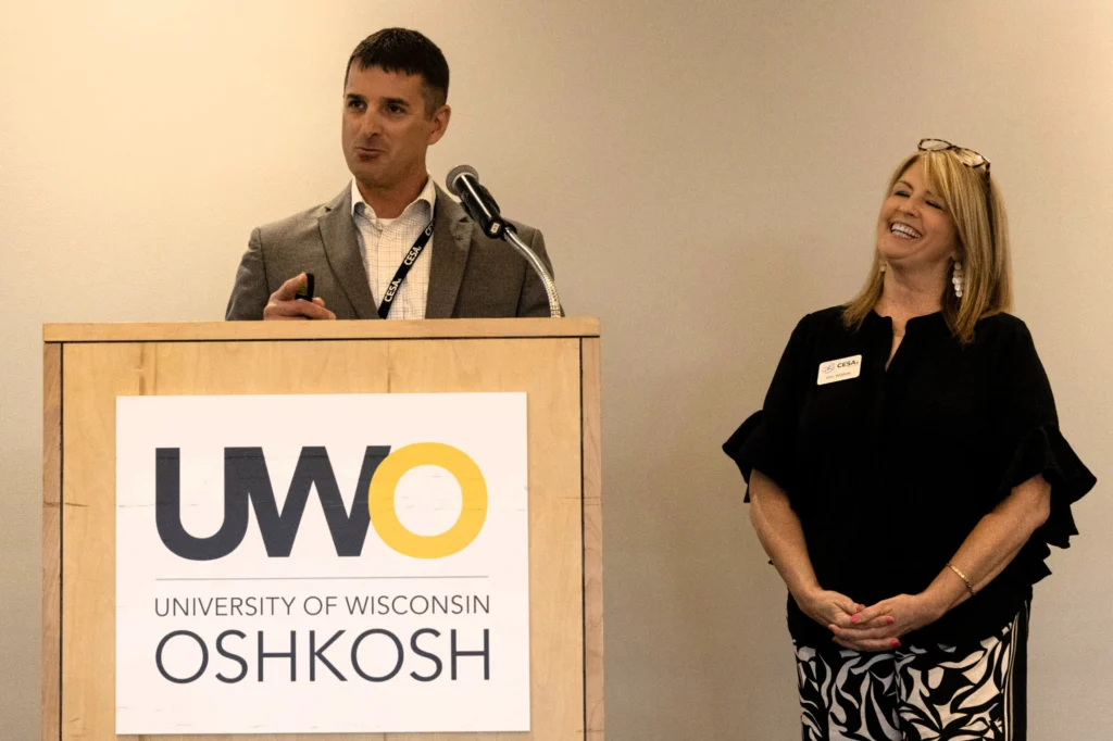 Two professionals at a University of Wisconsin Oshkosh podium, man speaking and woman smiling.