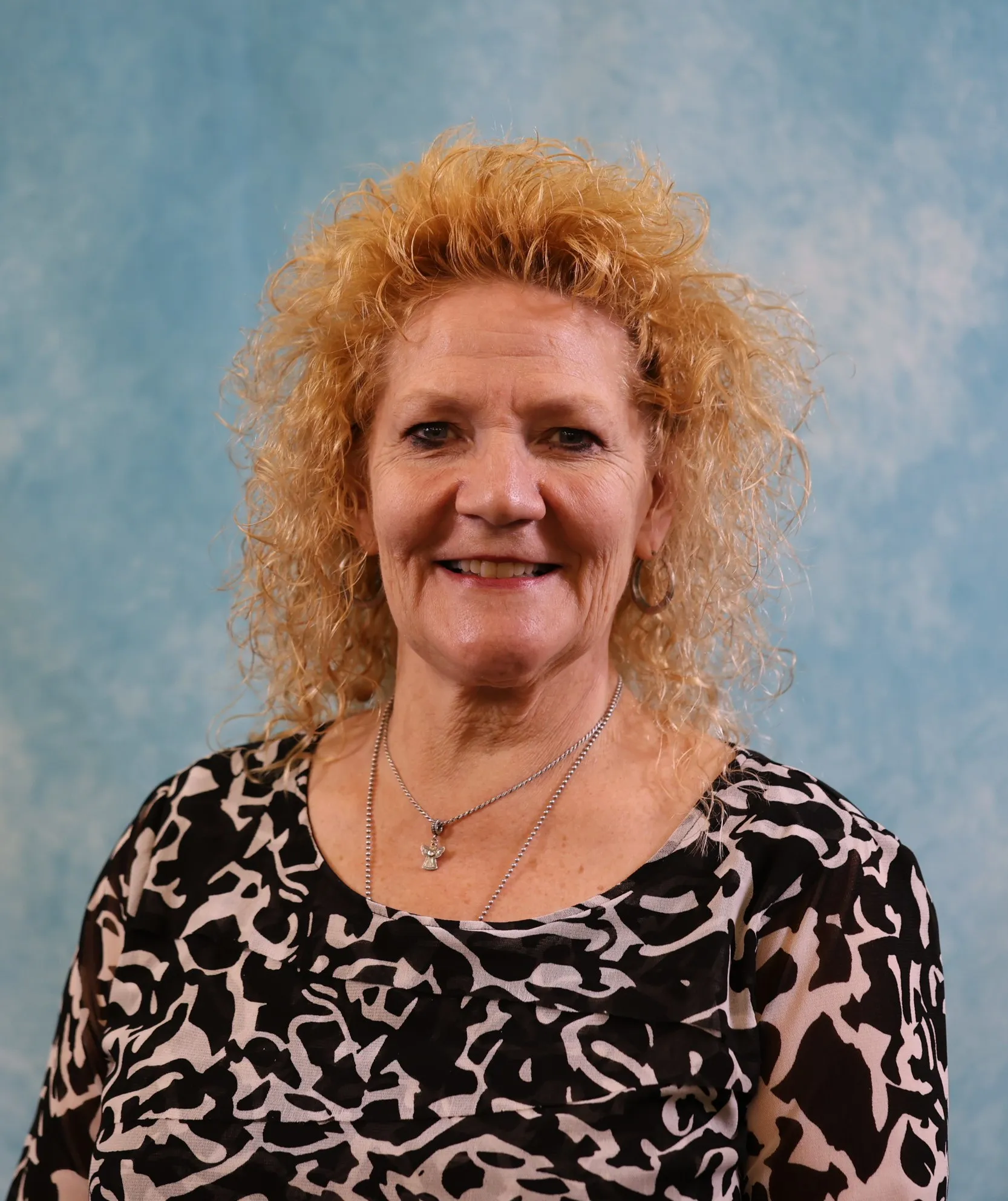 Portrait of a smiling middle-aged woman with curly blonde hair and patterned blouse.