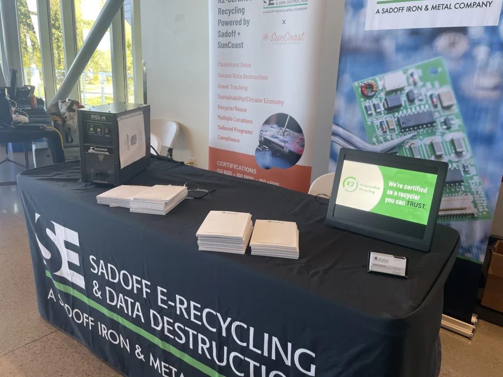 Exhibition table with Sadoff E-Recycling branding, informational brochures, and digital display.