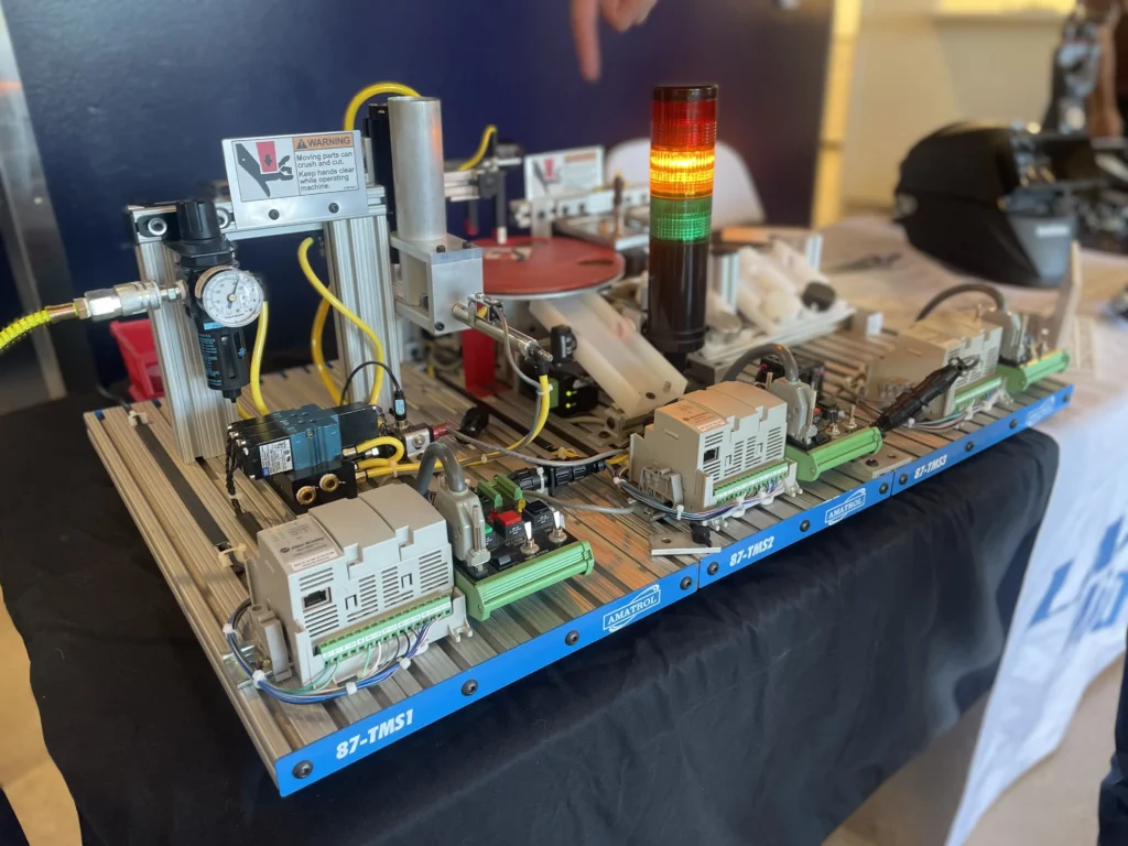 Industrial automation training setup with control modules, wiring, pressure gauge, and warning label.