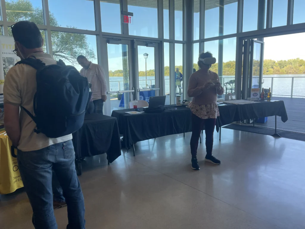 Indoor event with people near tables and a woman wearing a virtual reality headset.