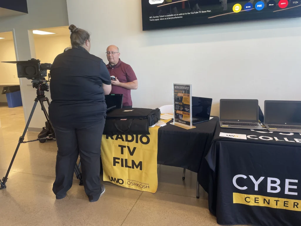 Two people conversing at University of Wisconsin Oshkosh Radio TV Film and Cyber Center informational tables.