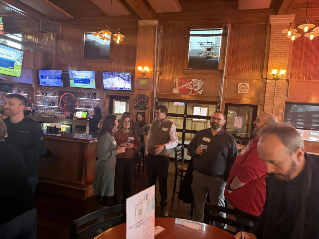 Group of professionally dressed adults socializing in a warmly lit wooden bar interior.