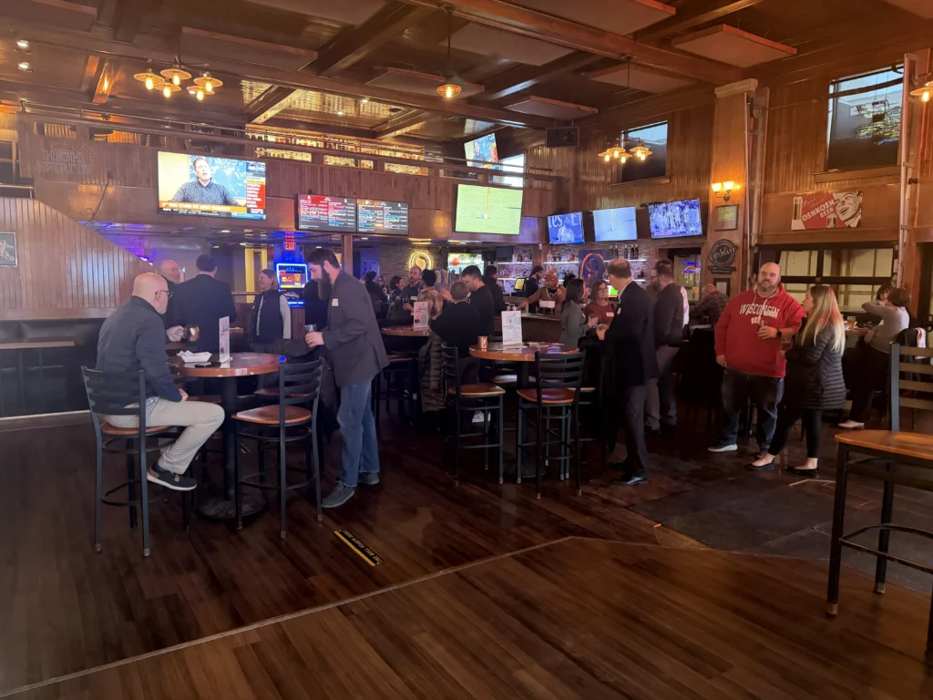 Interior of a busy, wood-paneled bar with patrons socializing and multiple televisions displaying sports.