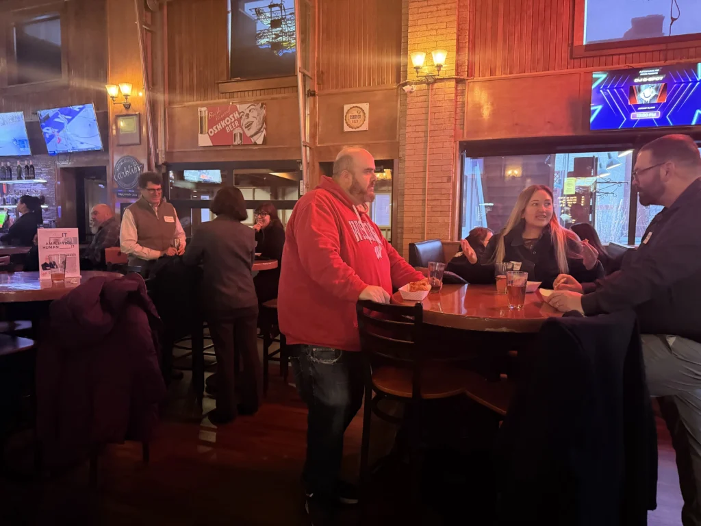 Group of people socializing and drinking in a warmly lit bar with wooden decor.