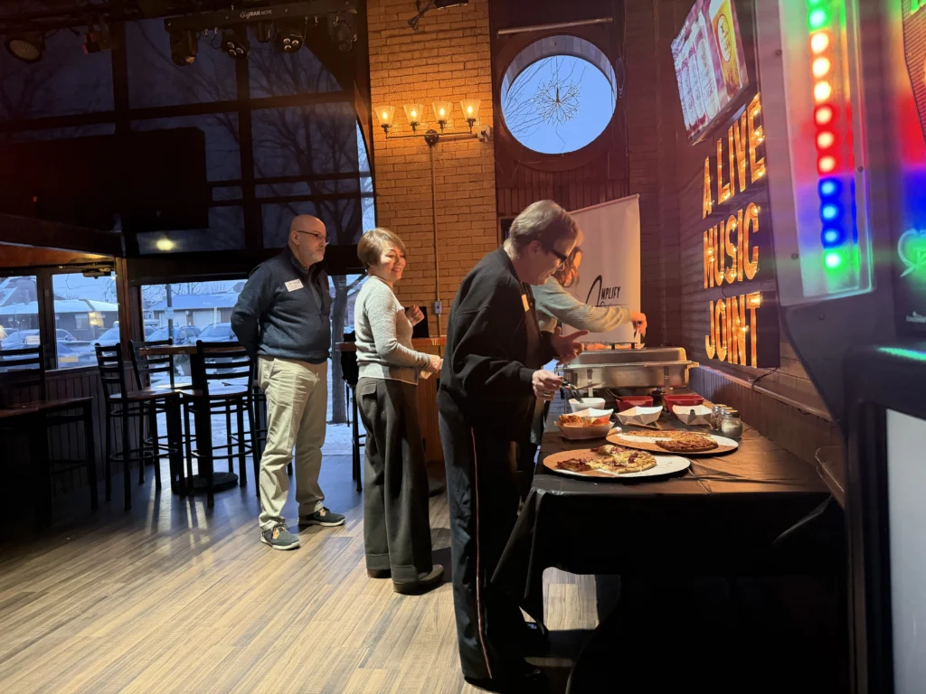 Four adults serving themselves food from a buffet table inside a dimly lit restaurant with a "Live Music Joint" illuminated sign.