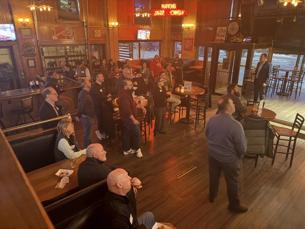 Adult audience attentively listening to a speaker in a warmly lit bar with wooden interiors.