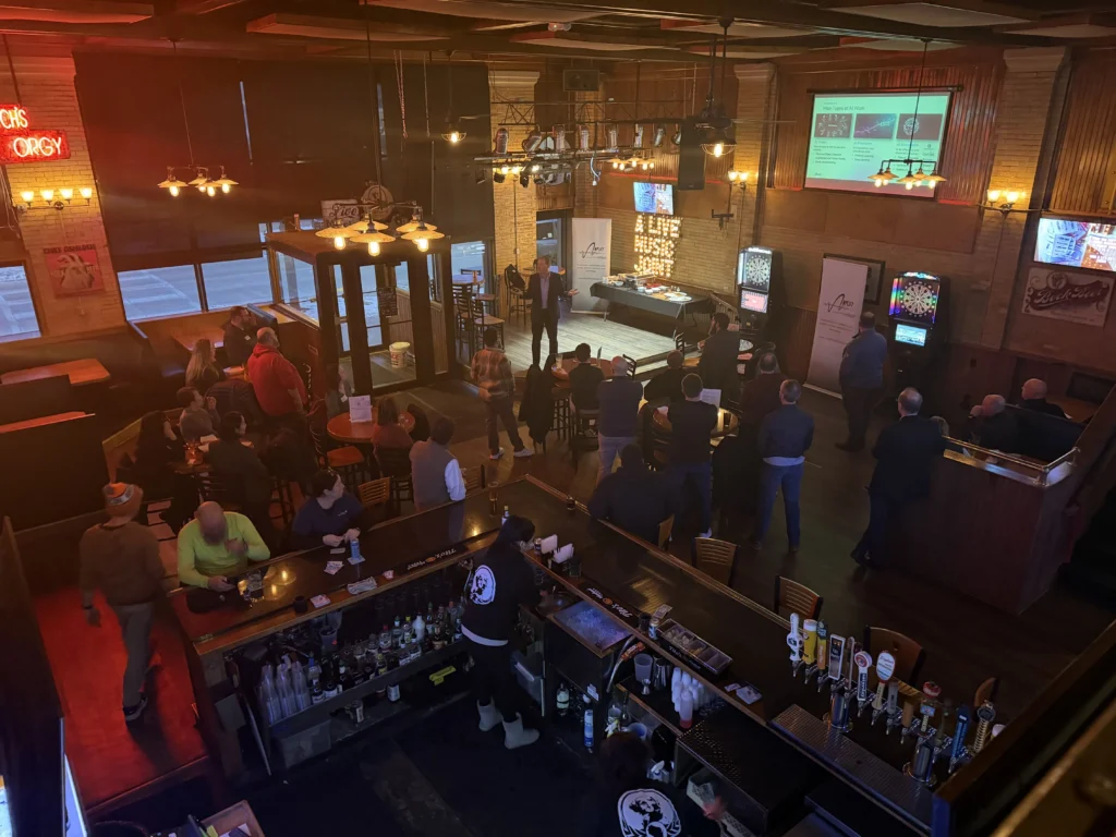Interior view of a bar with patrons watching a speaker presenting a slide on AI work types.