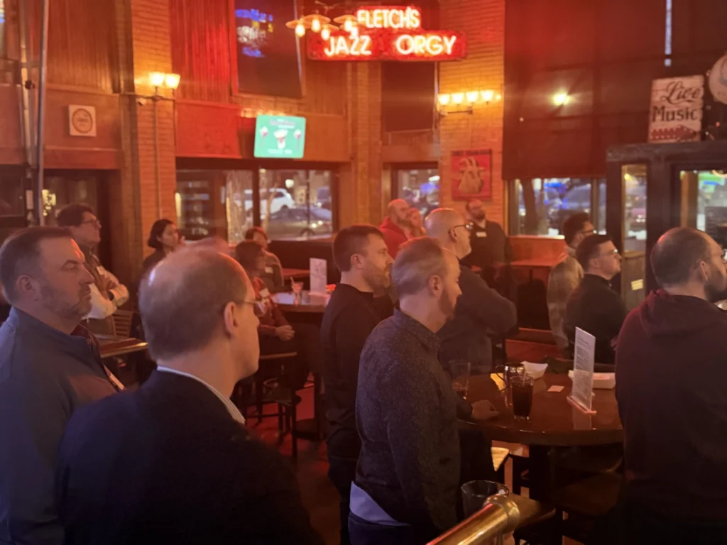 Group of people attentively watching an event inside a dimly lit bar with red neon signs and wooden interior.