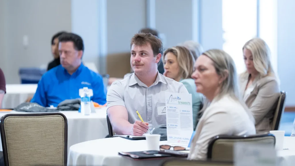 Group of adults seated at round tables attending a professional seminar or workshop in a conference room.