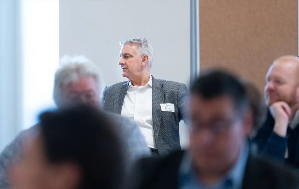 Middle-aged man in gray blazer with name tag looking to his left during conference.