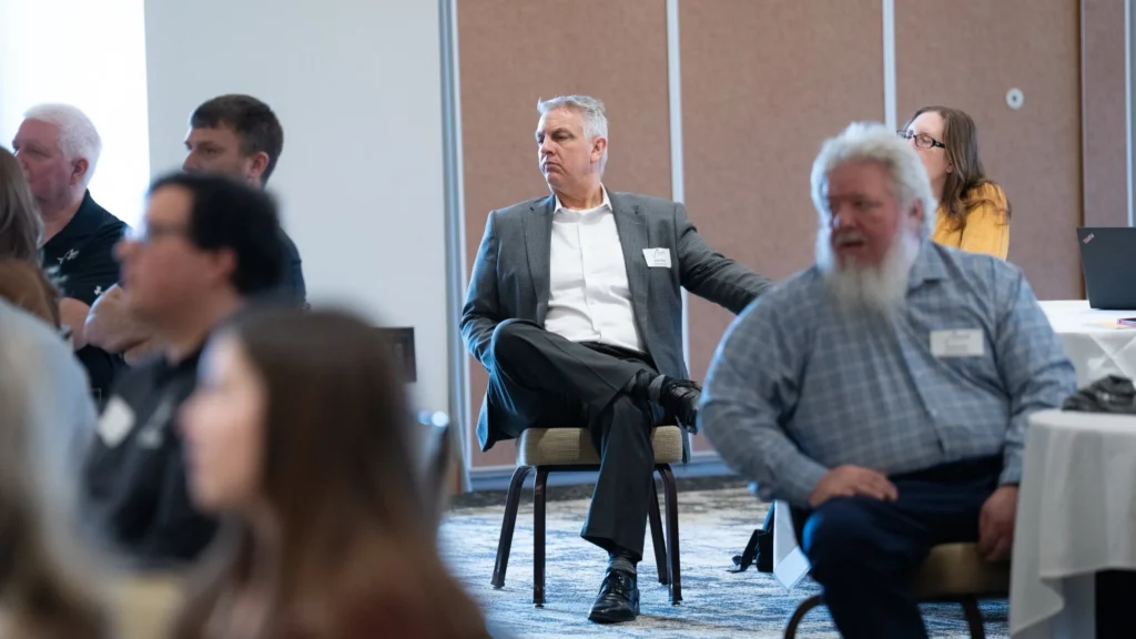Group of professionally dressed adults seated and attentively listening in a conference room.