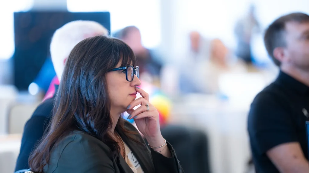 Woman with dark hair and glasses attentively listening in a professional meeting setting.
