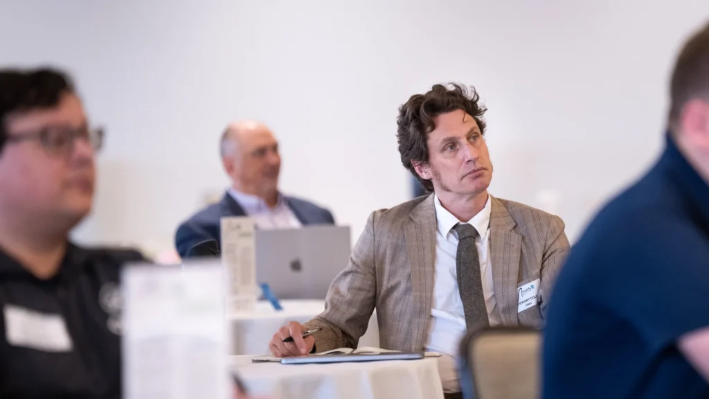 Professional men attentively listening at a conference table, one with a notebook and pen.