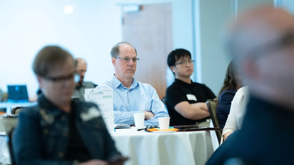 Group of professionals attentively seated at round tables in a conference room.