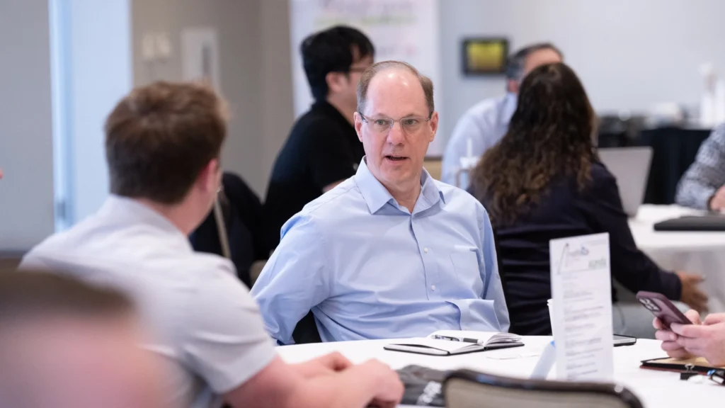 Middle-aged man in glasses and blue shirt conversing at a professional meeting table.