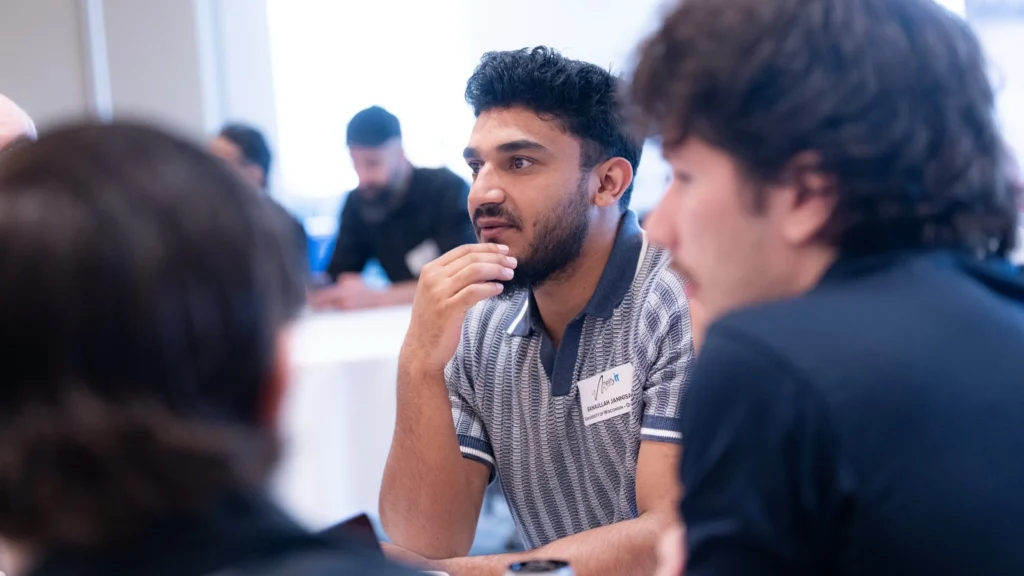 Young man in striped polo shirt attentively listening during group discussion at conference.