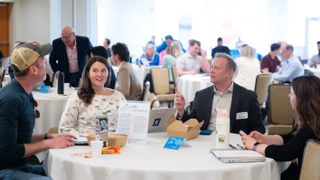 Professionally dressed group of four adults engaged in discussion at a round conference table.