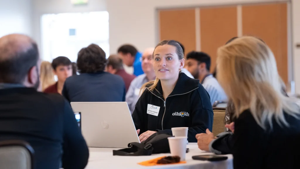 Professional woman wearing a black Discover Oshkosh jacket engaged in discussion at a conference table.