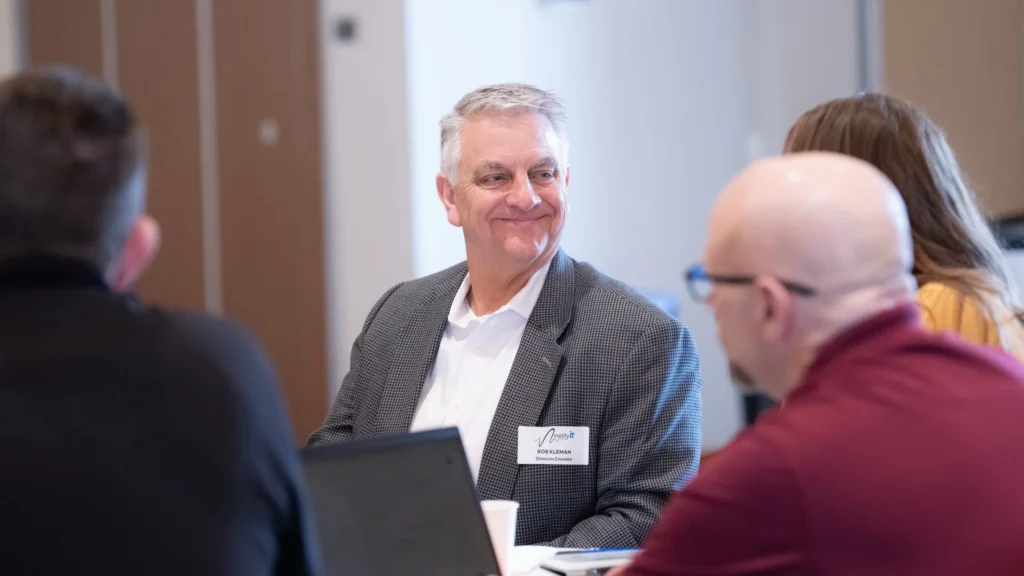 Middle-aged man in gray suit jacket with name tag smiling during a professional meeting.