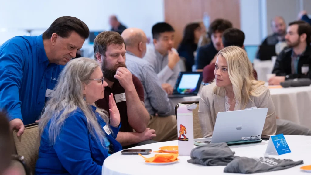Group of professionals engaged in discussion around a table with laptop and water bottle.