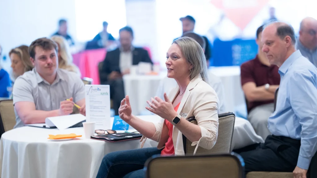 Professionally dressed individuals engaged in discussion around a round table in a conference setting.