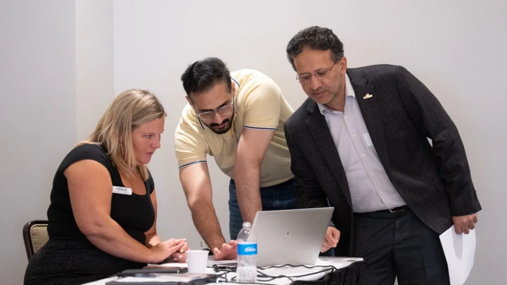 Three professionals, two men and one woman, collaborating over a laptop in a meeting room.