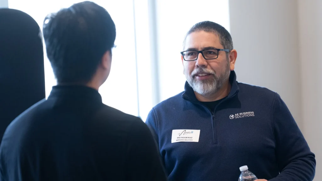 Two men engaged in conversation, one wearing AE Business Solutions attire and holding a water bottle.