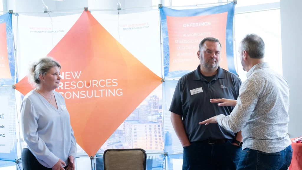 Three professionals conversing at a New Resources Consulting booth with orange and blue promotional banners.