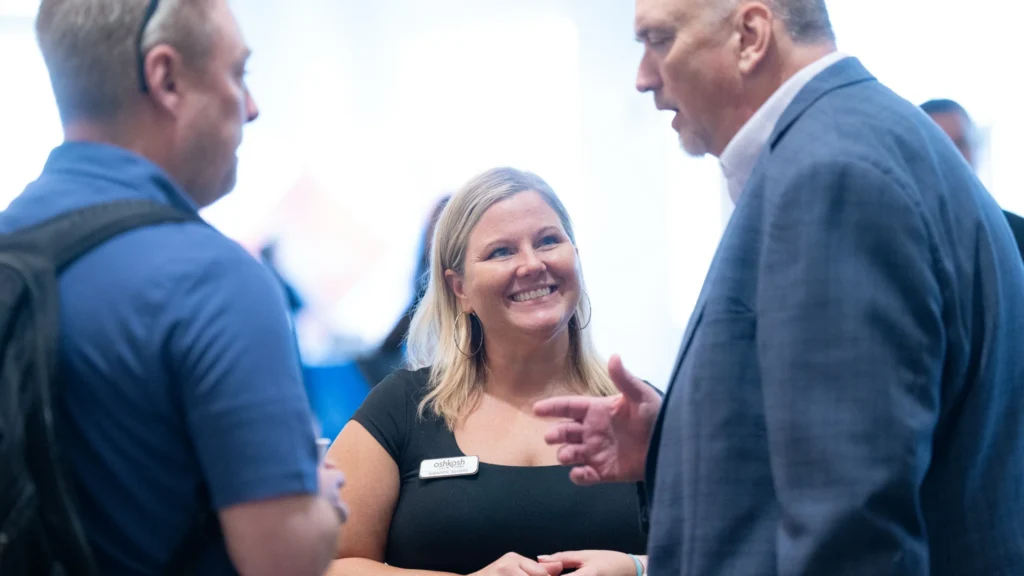 Three professionals engaged in conversation, with a smiling woman wearing a black dress and name tag.