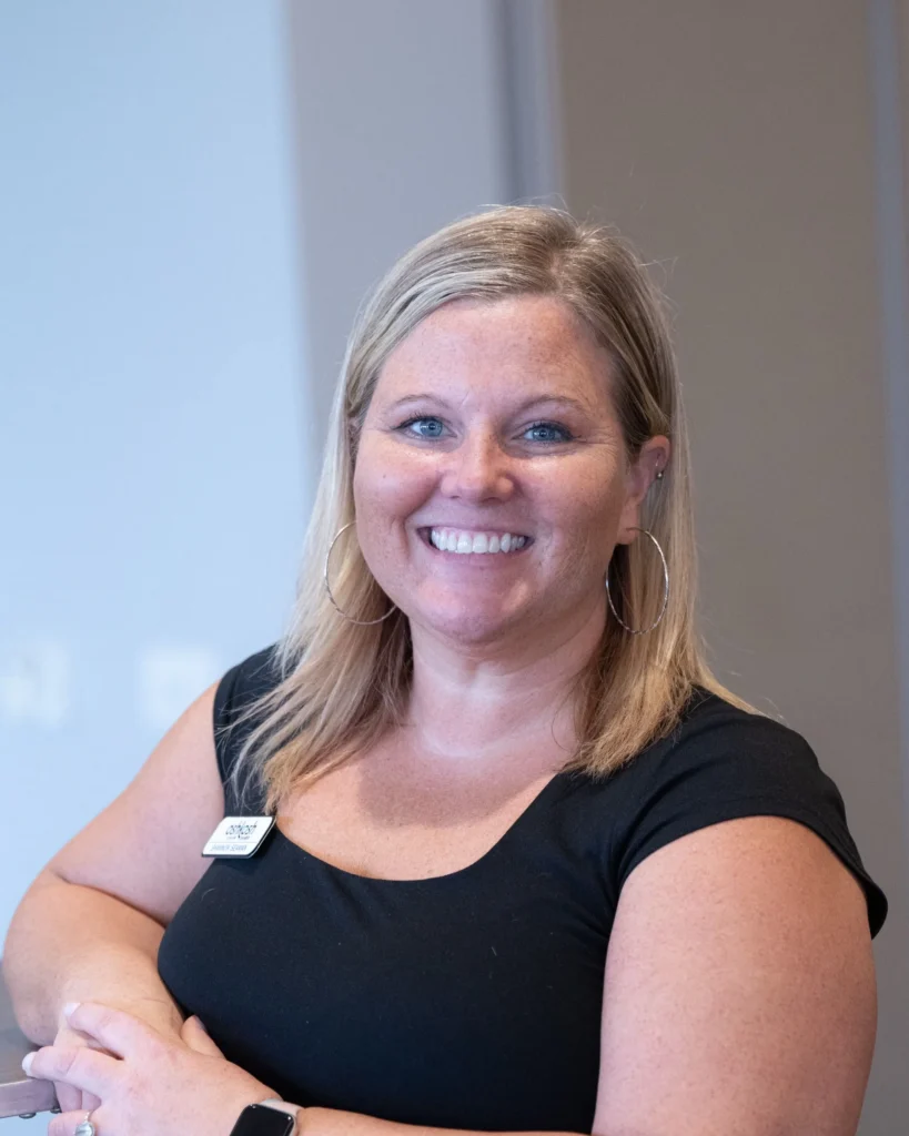 Professional woman with blonde hair, wearing a black top and hoop earrings, smiling indoors.