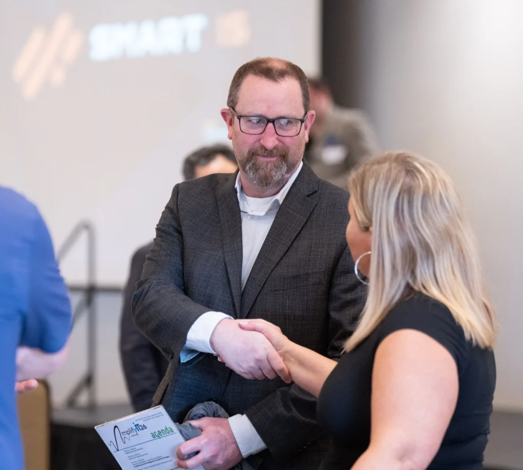 Man in dark suit shaking hands with woman in black dress at professional event.