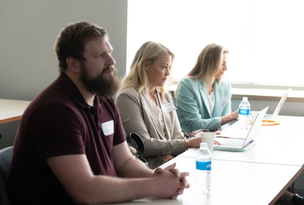 Three professionals seated at a table with laptops and water bottles, focused on work.