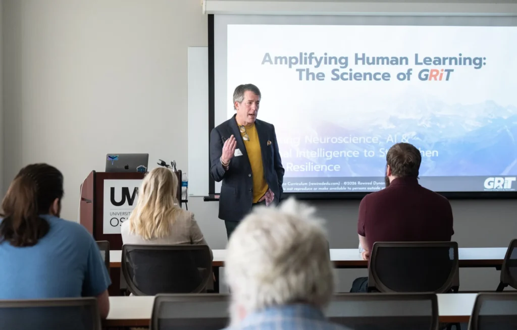 Presenter speaking to audience in classroom with slide titled "Amplifying Human Learning: The Science of GRIT