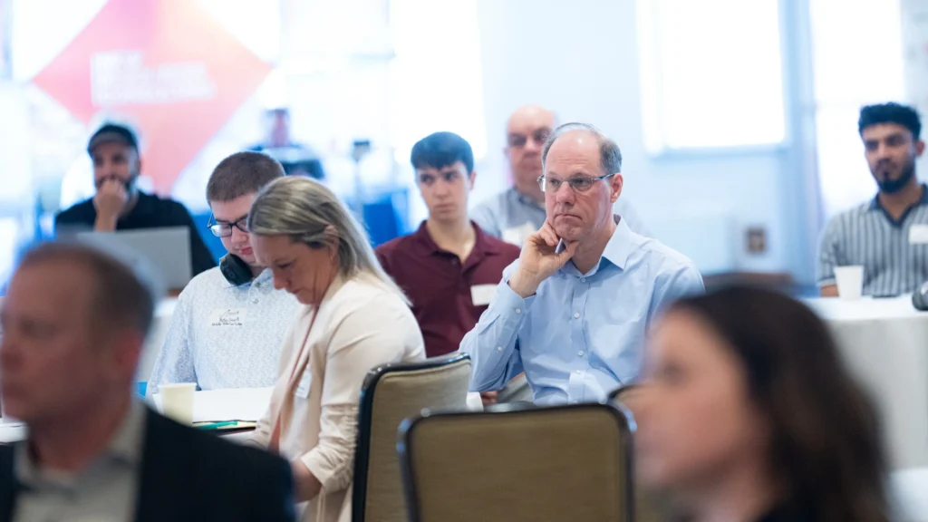Group of adults attentively listening in a bright conference room with white walls and large windows.