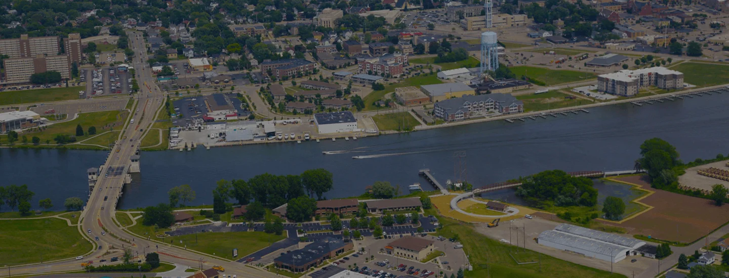 Aerial view of a riverside town with bridges, buildings, roads, and green spaces.