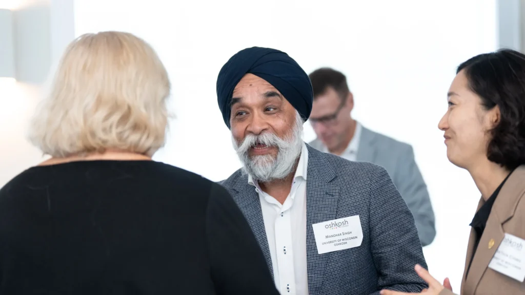 Professional group conversation featuring a man in a turban and name tag speaking with two women.