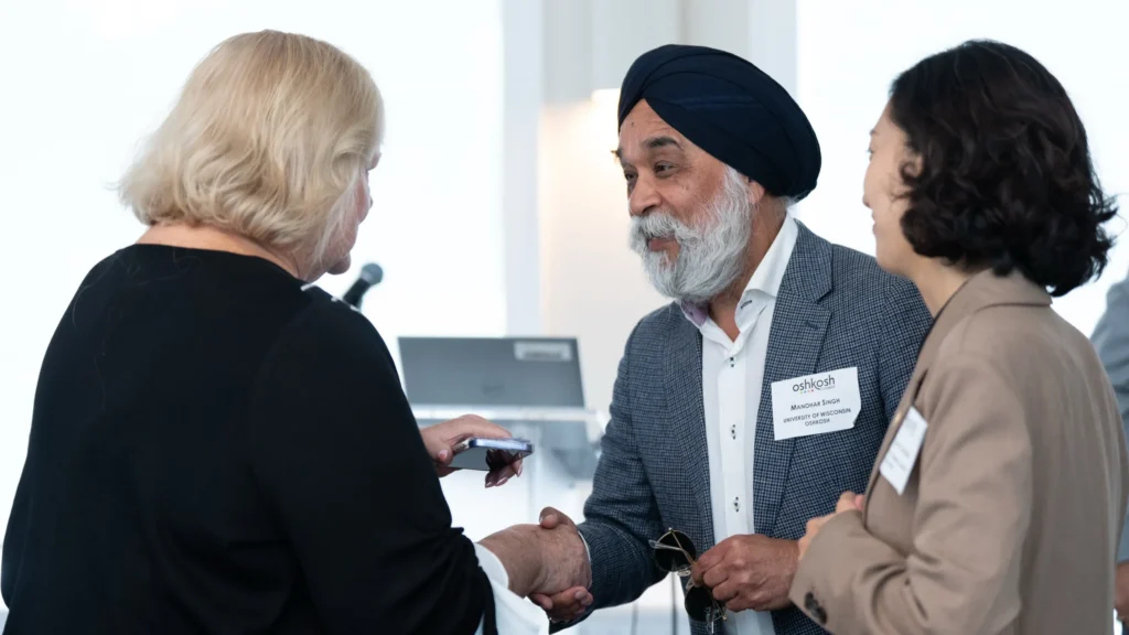 Three professionals engaged in conversation, with one man wearing a turban and name badge shaking hands.