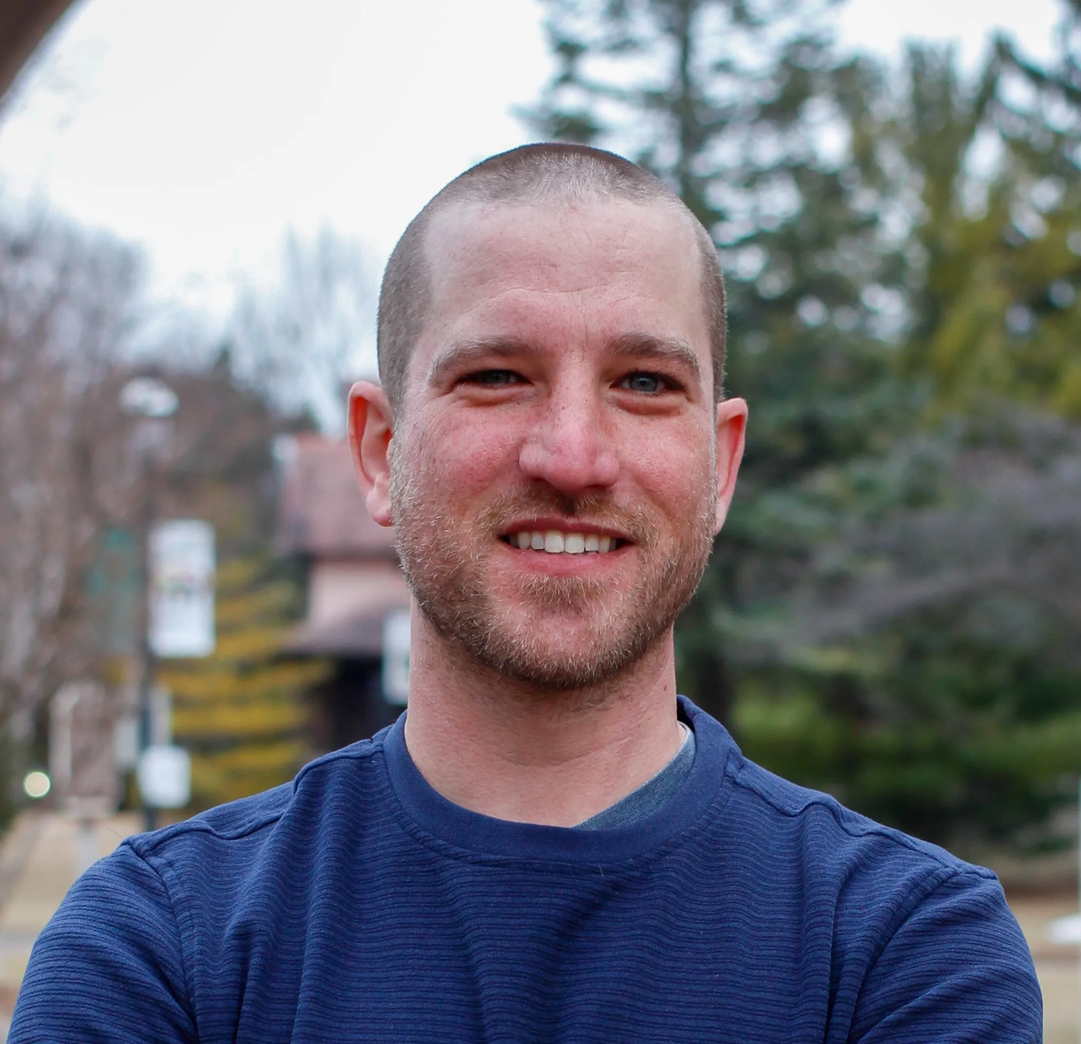 Portrait of a smiling man with short hair and beard wearing a blue sweater outdoors.