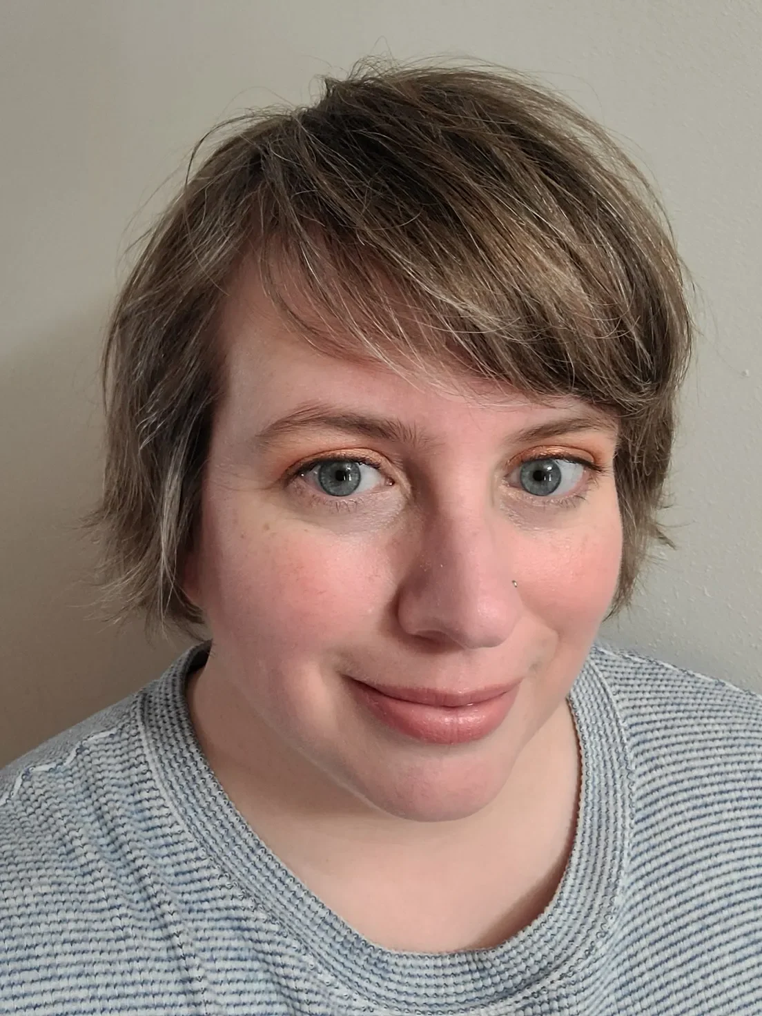 Close-up of a person with short light brown hair, blue eyes, and a gray knit sweater.